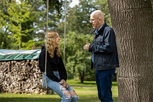 Eine junge Frau Sitzt auf einer an einem Baum hängenden Schaukel. Ein Mann steht vor ihr und spricht zu ihr. Eine junge Frau Sitzt auf einer an einem Baum hängenden Schaukel. Ein Mann steht vor ihr und spricht zu ihr.