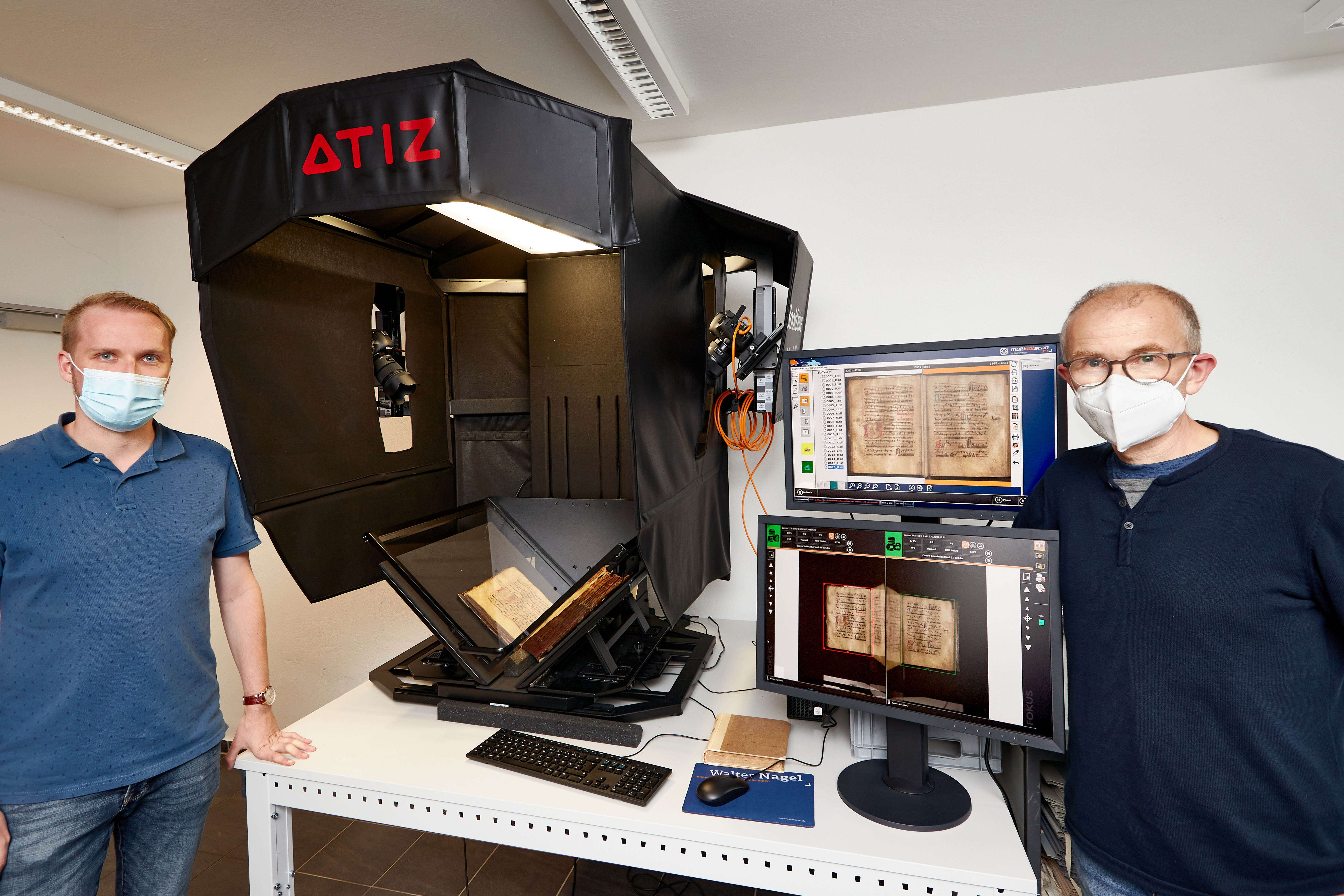 Lennart Metken und Stefan Jahn, Mitarbeiter des Bistumsarchiv, stehen links und rechts von dem nach oben aufgeklappten Scanner. Lennart Metken und Stefan Jahn, Mitarbeiter des Bistumsarchiv, stehen links und rechts von dem nach oben aufgeklappten Scanner.