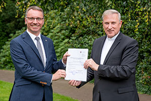 Weihbischof Wilfried Theising überreicht Dr. Markus Wonka eine Urkunde.