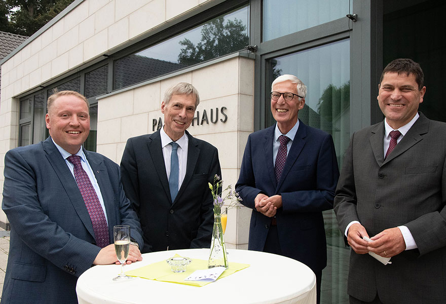 Pfarrer David Formella, Dr. William Middendorf, Leiter der Hauptabteilung Schule und Erziehung im Bistum Münster, Thomas Birkenhauer und der neue Schulleiter der Maristenschule, Stefan Schulze Beiering stehen um einen Stehtisch herum und lächeln in die Kamera.