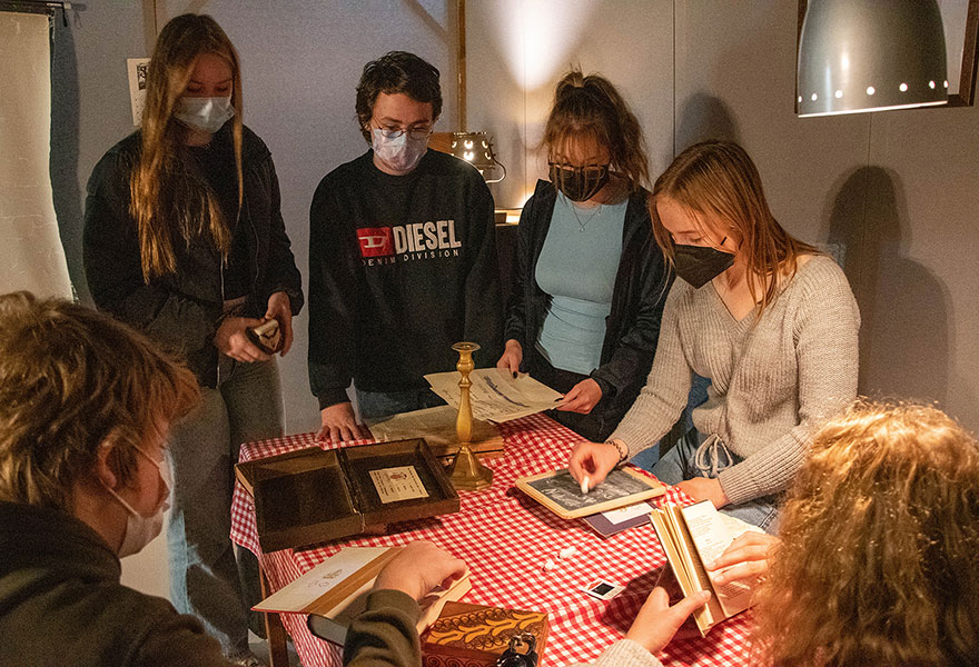 Schülerinnen und Schüler stehen um einen Tisch herum und blättern unter anderem in alten Büchern.