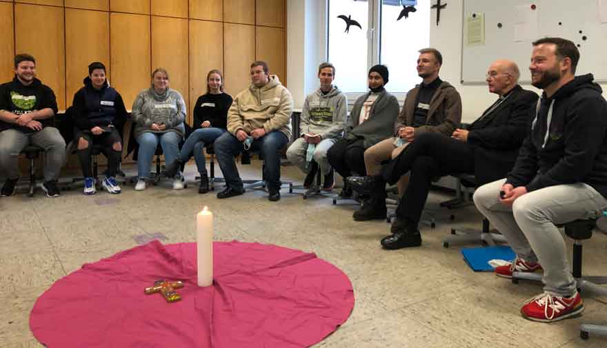 Mehrere Menschen sitzen um eine Kerze.