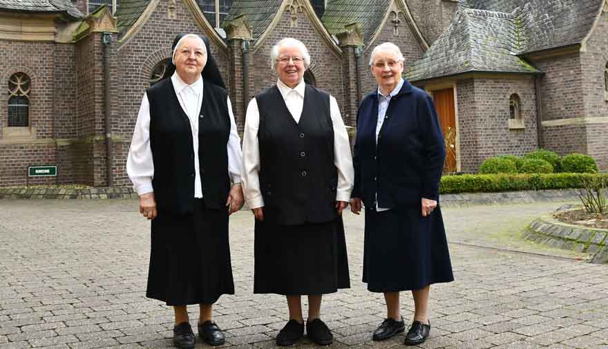 Drei Ordensschwestern stehen vor einer Kirche.