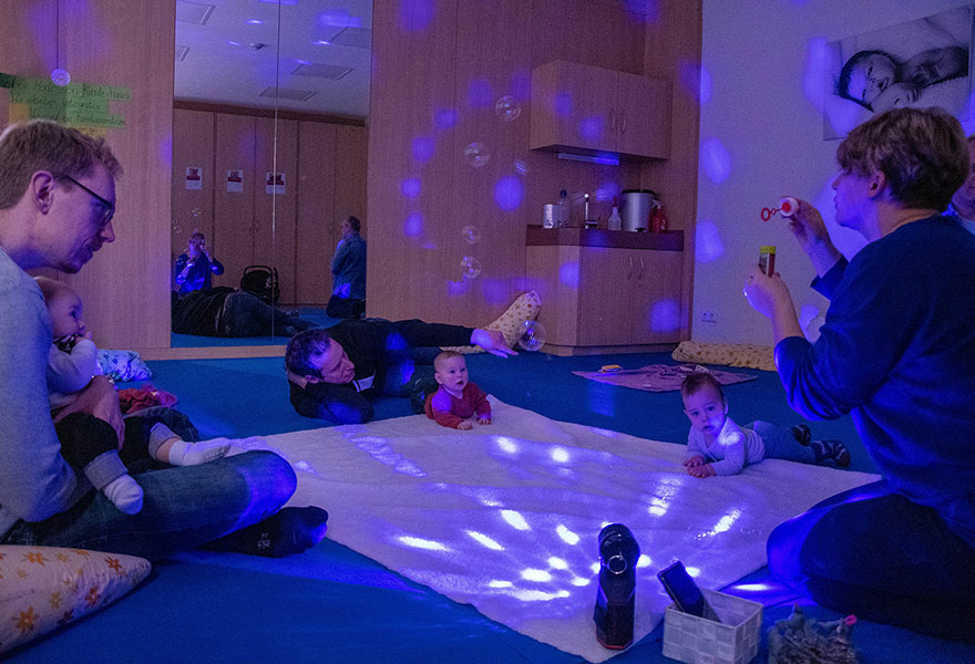 Babys liegen auf dem Boden und schauen fasziniert in buntes Licht und auf die Seifenblasen.