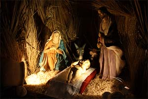 das Jesus-Kind liegt auf einem Kissen in einer aus Stroh gefertigten Krippe. Maria kniet rechts neben dem Kind, Josef steht auf der anderen Seite, beide schauen auf das Kind. Im Hintergrund stehen Ochs und Esel.