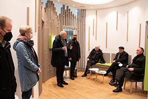 Hubert Schulte-Kemper erläutert dem Bischof und dem Weihbischof, die auf einer Bank Platz genommen haben, das Konzept des Kirchenpavillons im Marl.