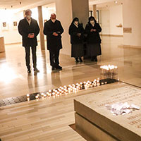 Vier Menschen stehen vor dem Grab, auf dem Zettel abgelegt sind, und beten. Vier Menschen stehen vor dem Grab, auf dem Zettel abgelegt sind, und beten.