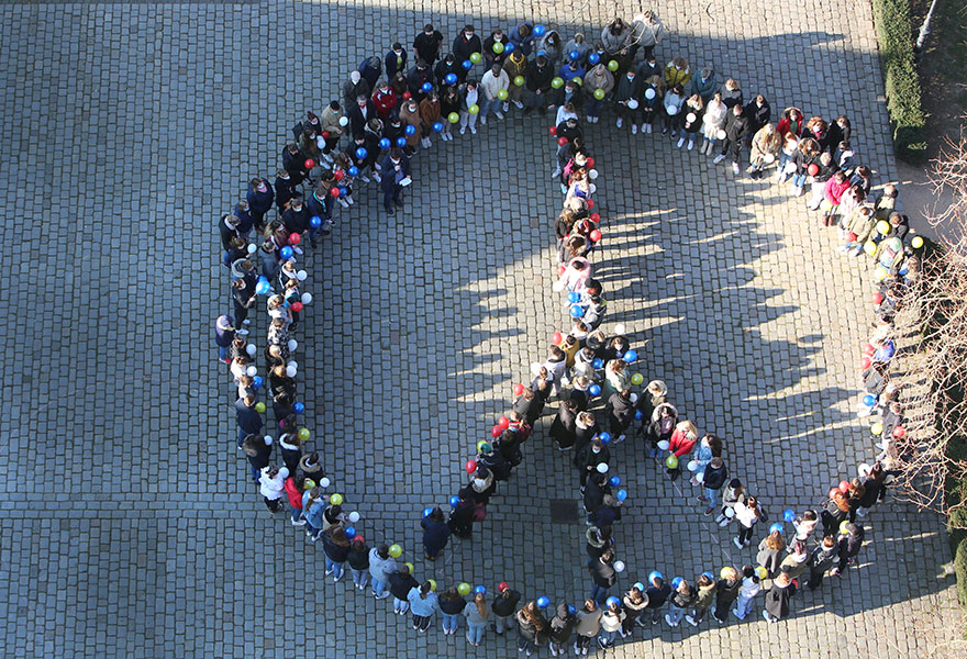 Viele Menschen stellen sich zu einem Peace-Zeichen auf, das von oben fotografiert ist.