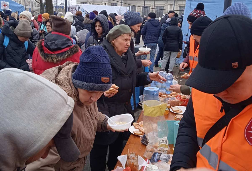 Menschen drängen sich um einen Tisch, an dem Essen ausgegeben wird.