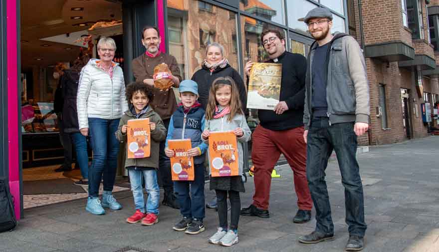 Drei Kinder und vier Erwachsene stehen vor einer Bäckerei.