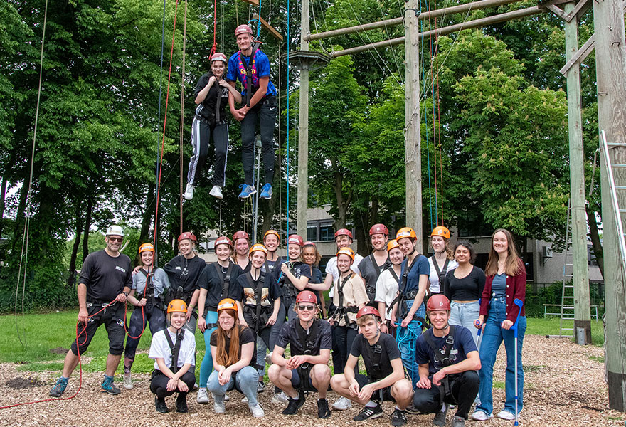 Die Freiwilligen haben sich zum Gruppenbild aufgestellt, zwei von ihnen hängen über ihnen an den Seilen.