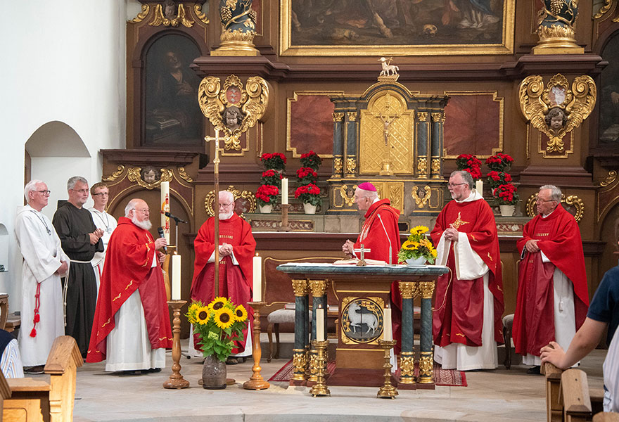 Im Altarraum der Kirche stehen die Kapuziner und der Bischof in roten Gewändern.