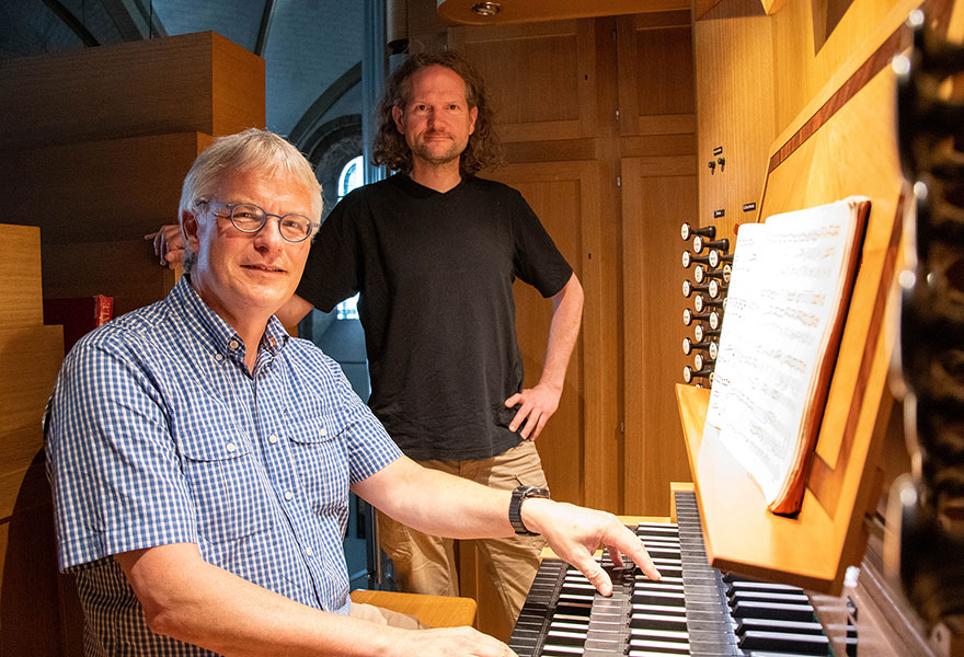 Ein Mann sitzt an der Orgel, im Hintergrund steht der Orgellehrer.