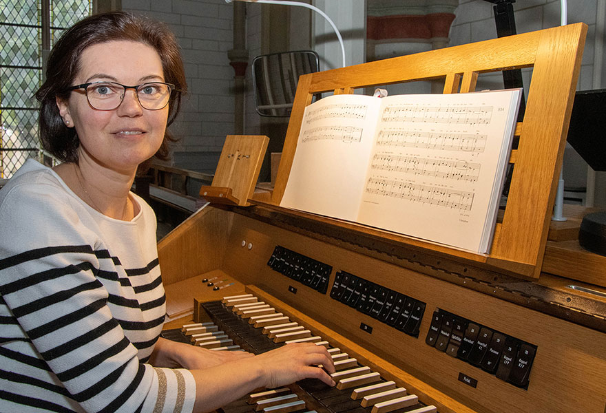 Eine Frau sitzt an einer Orgel und lächelt in die Kamera.