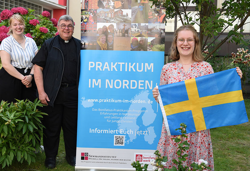 Johanna Müller hat eine kleine schwedische Fahne in der Hand. Im Hintergrund stehen Monsignore Georg Austen (Generalsekretär des Bonifatiuswerkes) und Marisa Grummich (Projektreferentin).