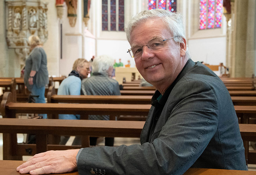 Johannes Arntz sitzt in einer Kirchenbank und lächelt in die Kamera. 