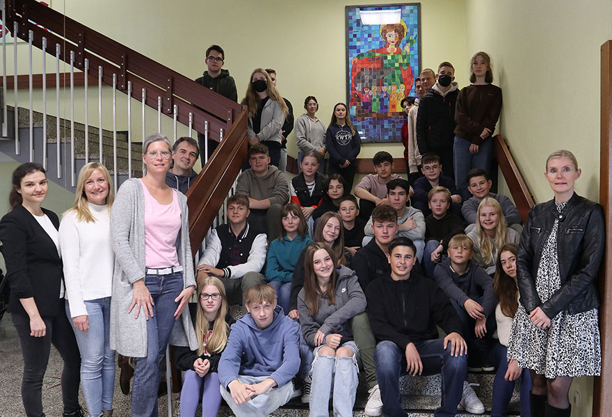 Schülerinnen und Schüler sowie Lehrerinnen und Lehrer haben sich auf einer Treppe zum Gruppenbild aufgestellt. Dahinter erkennt man das neue Mosaik.