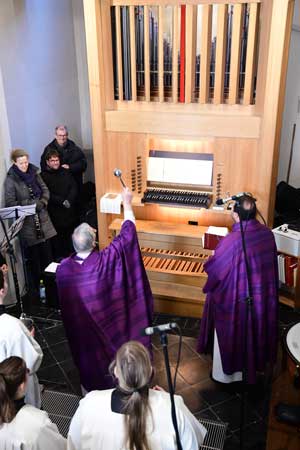 Zwei Priester stehen vor einer Orgel, einer schwenkt ein Weihrauchfass.