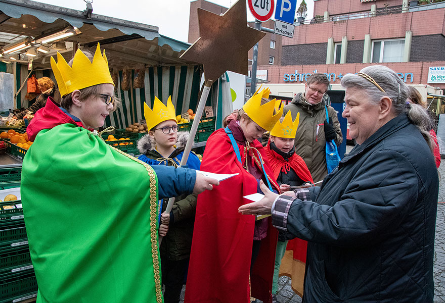 Sternsinger überreichen den Segensaufkleber an eine Frau.