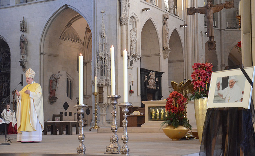 Blick in den Dom: Links sieht man Bichof Dr. felix Genn bei der Predigt, rechts im Vordergrund ist ein Bild des verstorbenen emeritierten Papstes mit Trauerschleife zu sehen. 