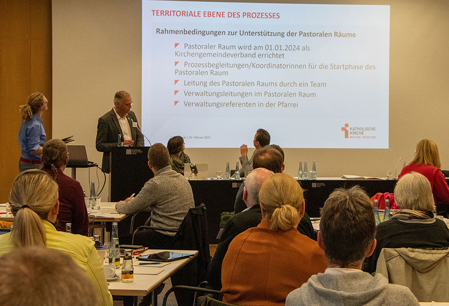 Im Saal sitzen die Delegierten und hören den Ausführungen von Generalvikar Dr. Klaus Winterkamp und Daniel Gewand zu, die entsprechende Folien an die Wand projizieren. 