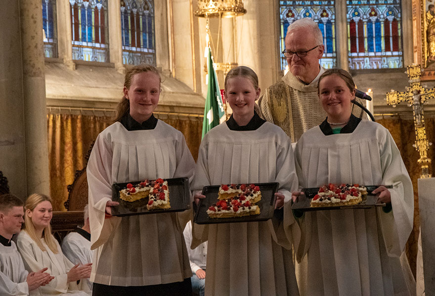 Drei Messdienerinnen halten jeweils einen Kuchen in Form einer Zahl in der Hand.