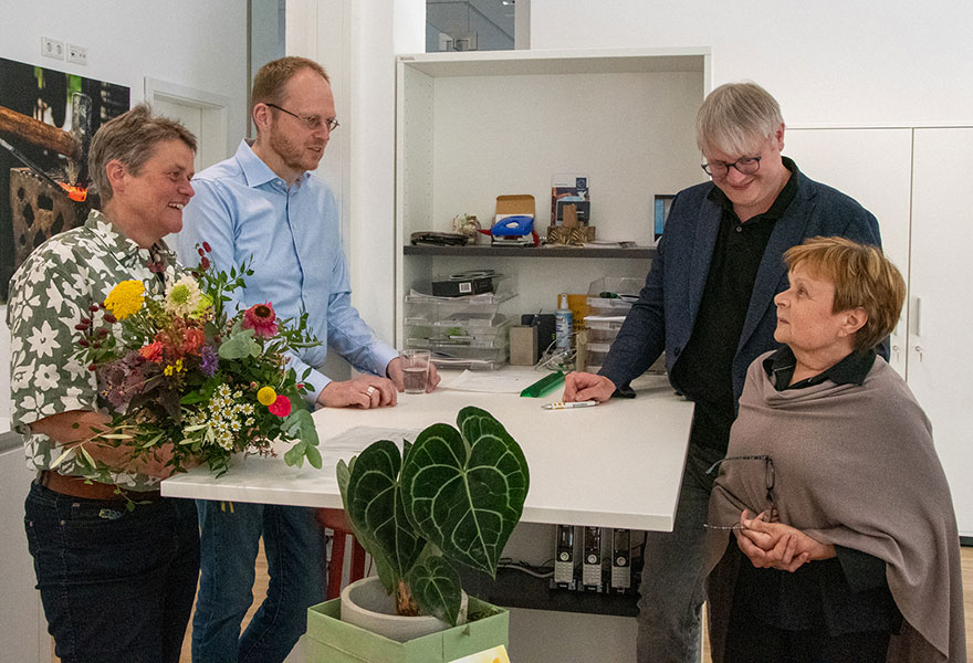 Vier Personen stehen an einem Tisch und sprechen miteinander.