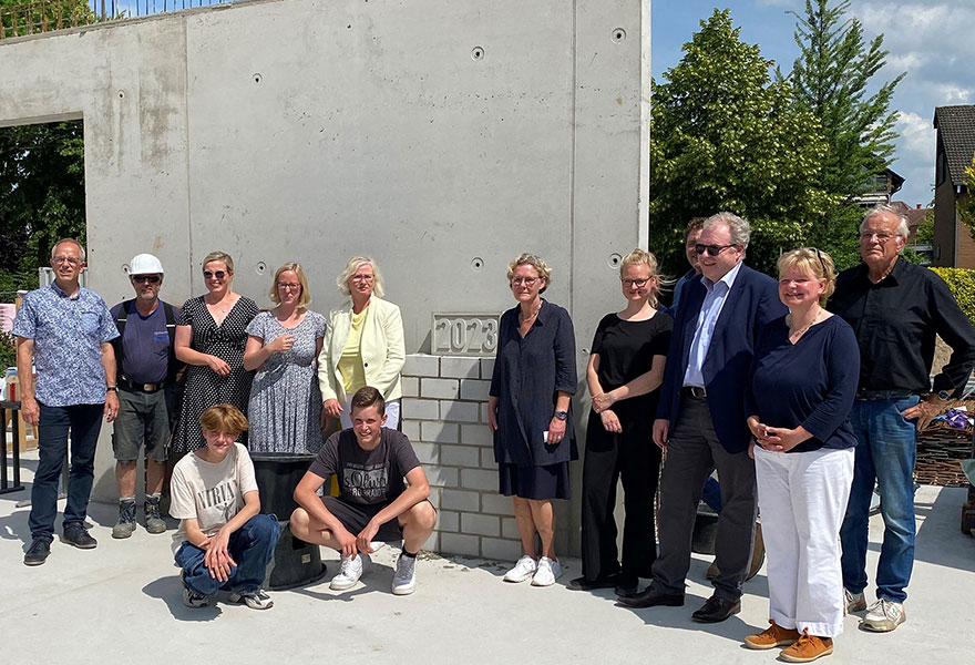 Eine Gruppe steht an einer gemauerten kleinen Wand, an der der Grundstein sichtbar ist.