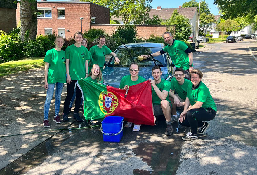 Eine Gruppe junger Menschen mit einer portugiesischen Fahne steht um ein Auto herum, das sie gewaschen haben.