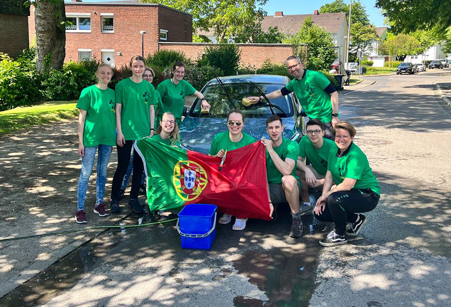 Eine Gruppe junger Menschen mit einer portugiesischen Fahne steht um ein Auto herum, das sie gewaschen haben. Eine Gruppe junger Menschen mit einer portugiesischen Fahne steht um ein Auto herum, das sie gewaschen haben.