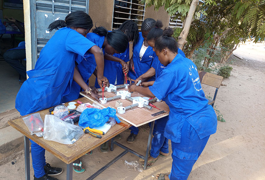 Frauen stehen in Burkina Faso um einen Tisch herum und schrauben an einem technischen Teil.