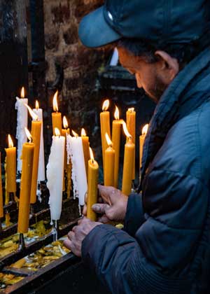 Ein Mann stellt eine Kerze auf einem Kerzenständer auf, auf dem schon weitere Kerzen brennen. Ein Mann stellt eine Kerze auf einem Kerzenständer auf, auf dem schon weitere Kerzen brennen.
