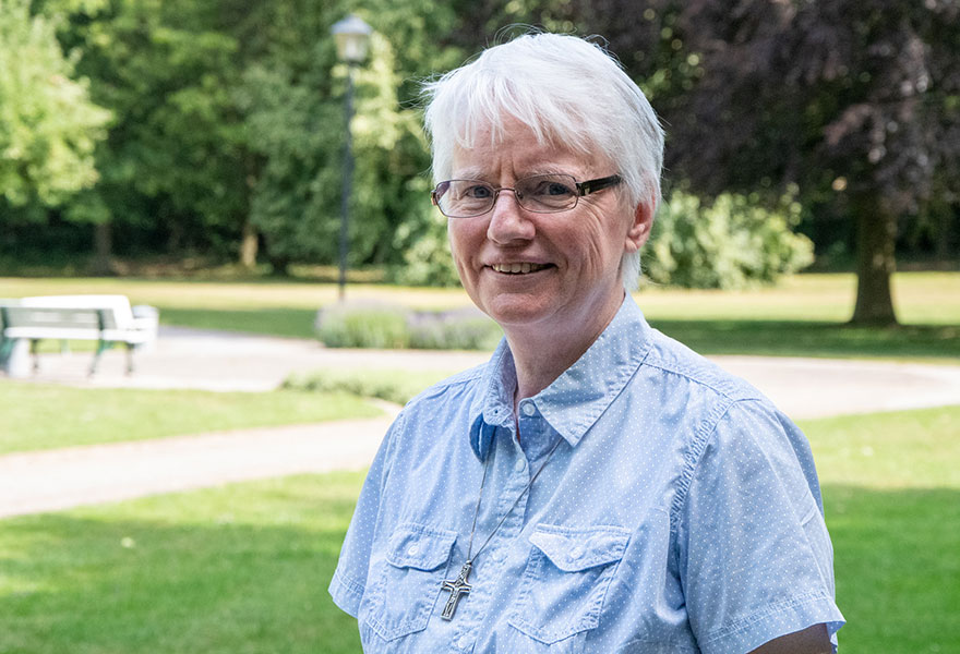 Schwester Paula steht im Klostergarten und lächelt in die Kamera.