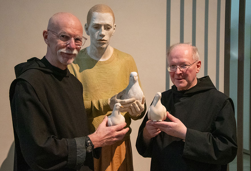 Links und rechts von der Statue stehen Pater Marcel und Bruder Liborius und halten jeweils eine der neuen Holztauben in der Hand.