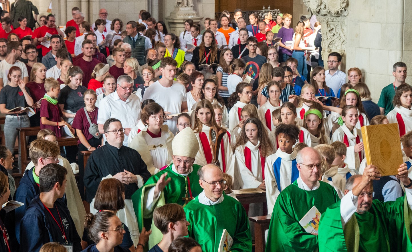 Der Bischof und weitere Beteiligte ziehen durch den Mittelgang des mit jungen Menschen voll besetzten Dom ein.