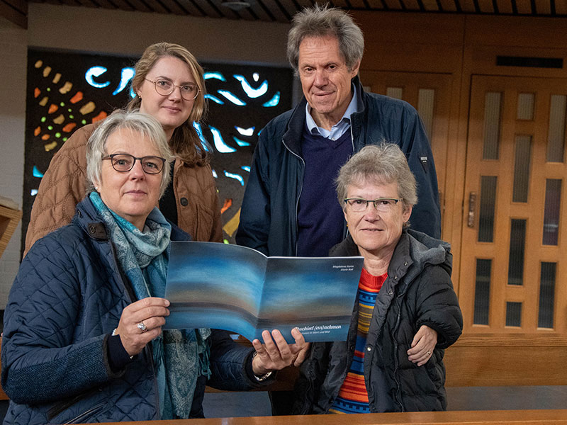 Die Beteiligten sitzen in einer Kirchenbank und lächeln in die Kamera.