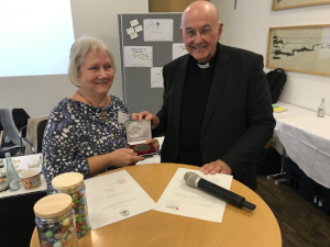 Brigitte Lehmann und Bischof Felix Genn stehen nebeneinander an einem Stehtisch und präsentieren lächelnd die Paulusplakette.