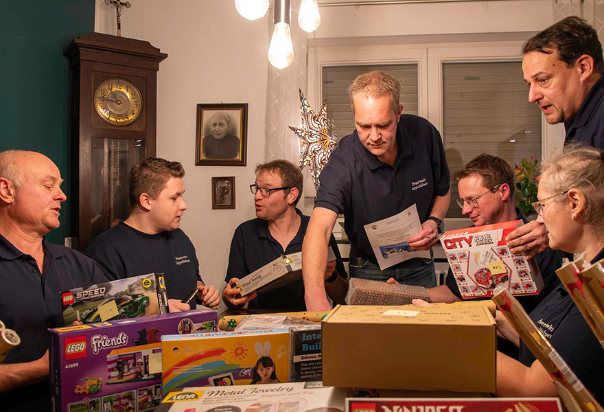 Die Feuerwehrleute sitzen um einen Tisch herum und packen Geschenke ein.