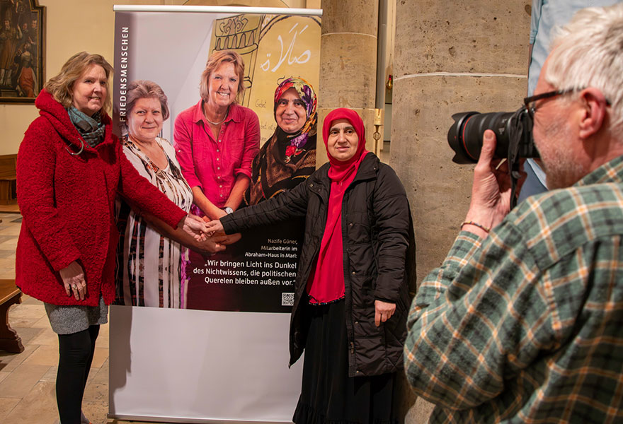 Zwei Frauen stehen links und rechts an einem großen Foto und werden von dem Fotografien fotografiert.