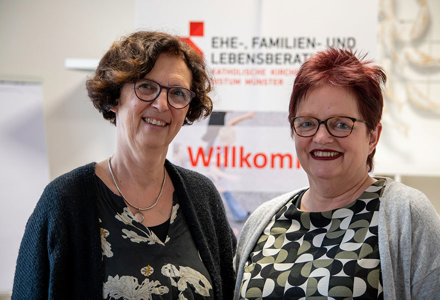 Die beiden Frauen stehen nebeneinander und lächeln in die Kamera´.