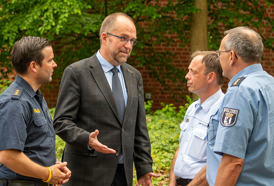 Vier Männer, davon drei in Polizeiuniform, stehen zusammen und unterhalten sich.