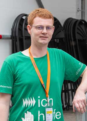 Ein Mann mit einem grünen T-Shirt lehnt sich mit einem Arm auf ein Geländer.