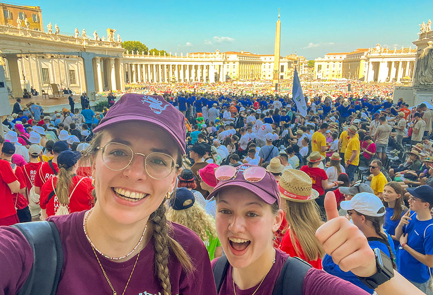 Zwei junge Frauen machen ein Selfie, auf dem hinter ihnen viele Menschen auf dem Petersplatz zu sehen sind. Zwei junge Frauen machen ein Selfie, auf dem hinter ihnen viele Menschen auf dem Petersplatz zu sehen sind.