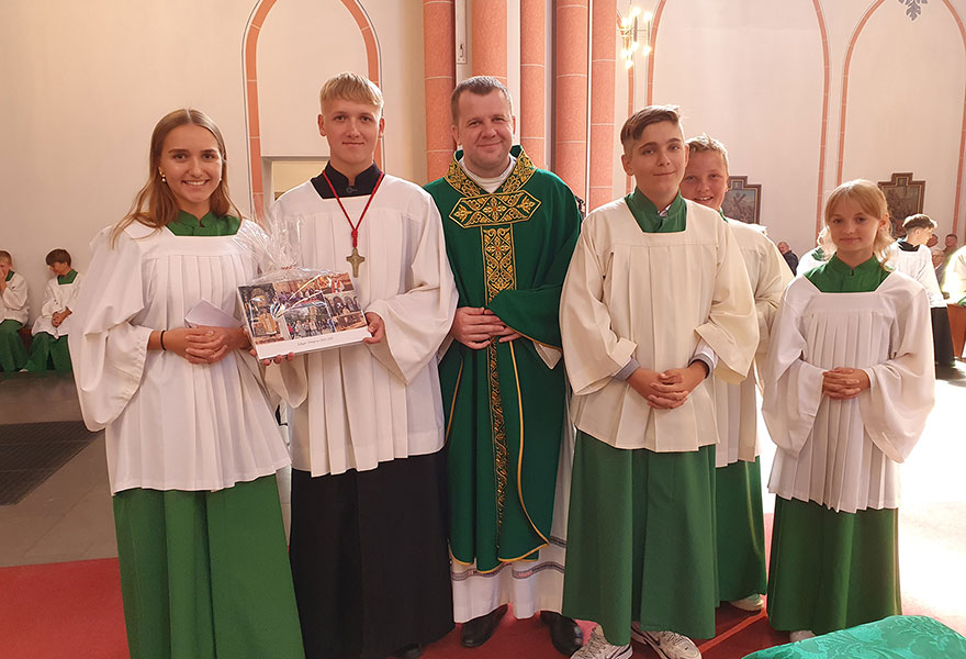 In der Mitte steht der Priester. Rechts und links von ihm stehen Messdienerinnen und Messdiener.