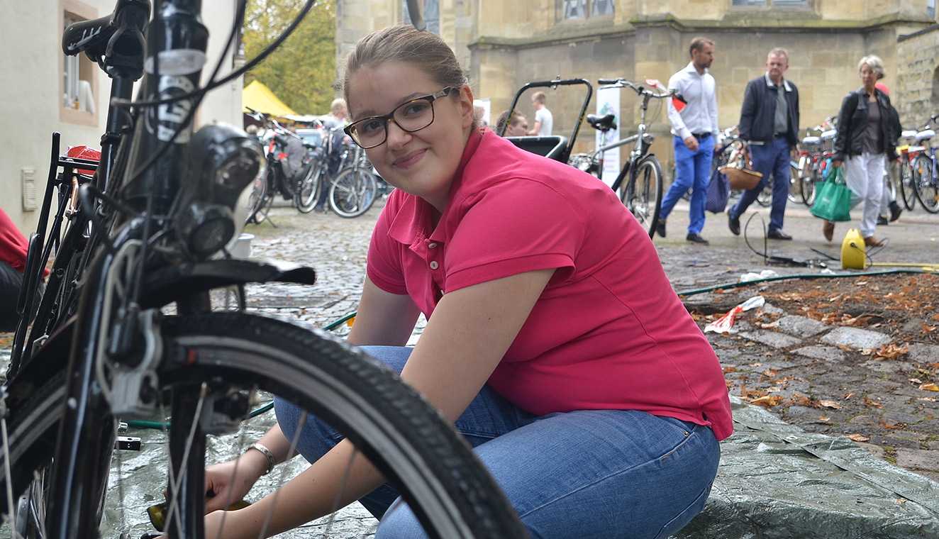 Eine junge Frau putzt ein Fahrrad und lächelt freundlich in die Kamera.