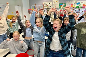 Schülerinnen und Schüler springen auf und reißen die Arme in die Luft. Schülerinnen und Schüler springen auf und reißen die Arme in die Luft.
