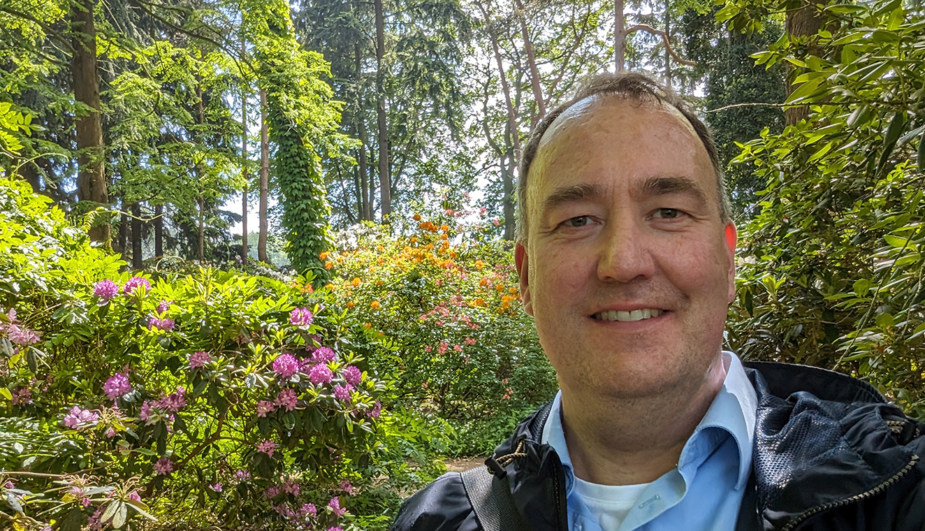 Stefan von Ühm steht draußen im Hintergrund blüht eine violette Hortensie.
