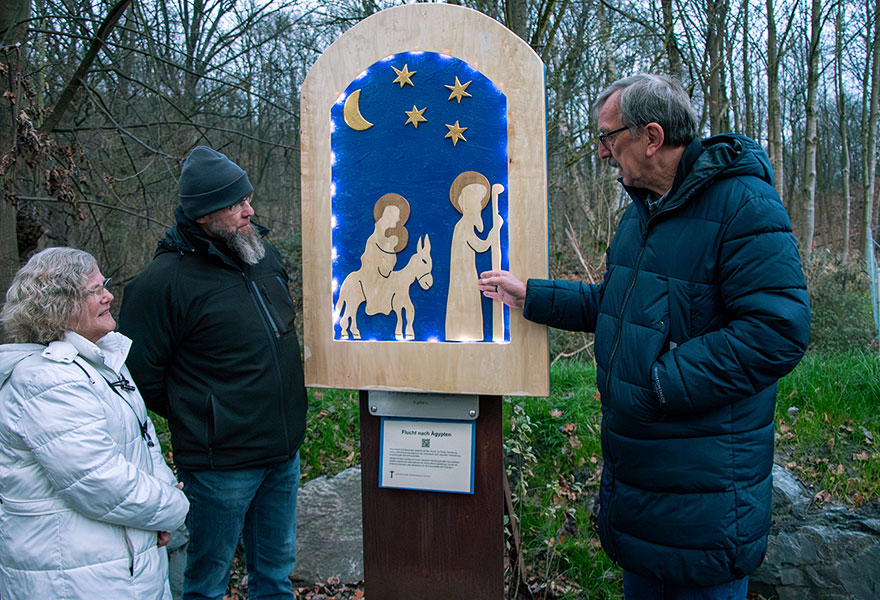 An einer Darstellung, die beleuchtet ist, stehen die Beteiligten und schauen sich das Bild an.