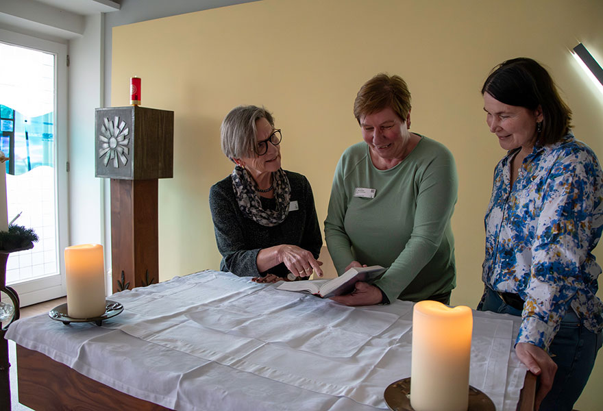 Drei Frauen stehen um einen Altar herum und schauen in das Gotteslob.