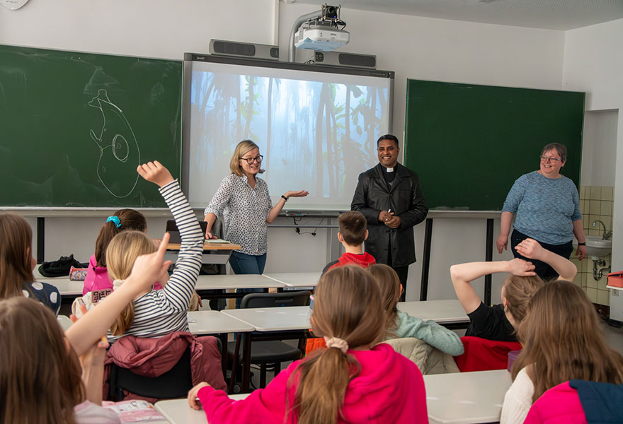 Vor der Tafel stehen die Beteiligten. Zahlreiche Schülerinnen und Schüler heben ihre Finger, um eine Frage zu stellen.